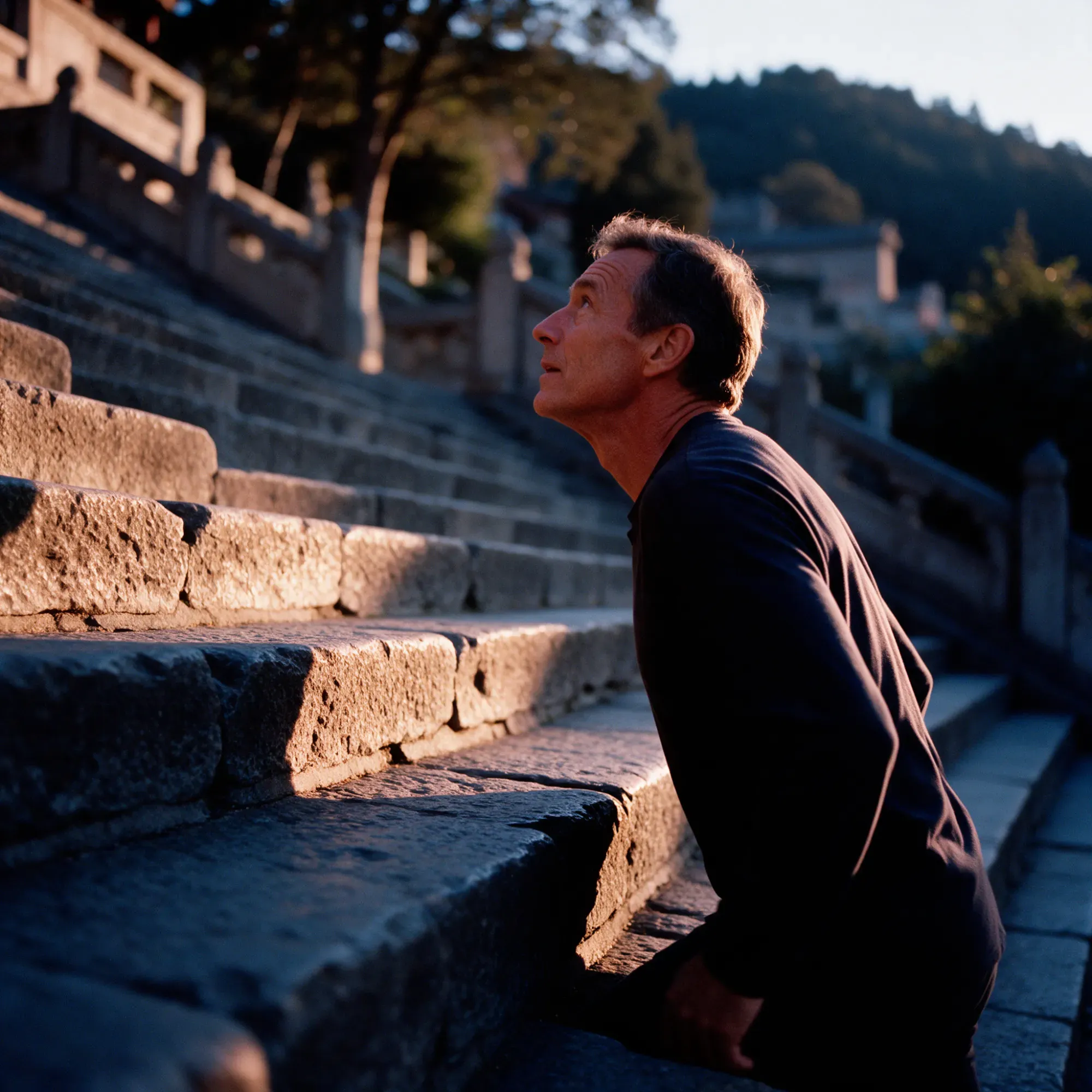 A man in his mid-fifties on a long flight of outdoor stone steps in morning light