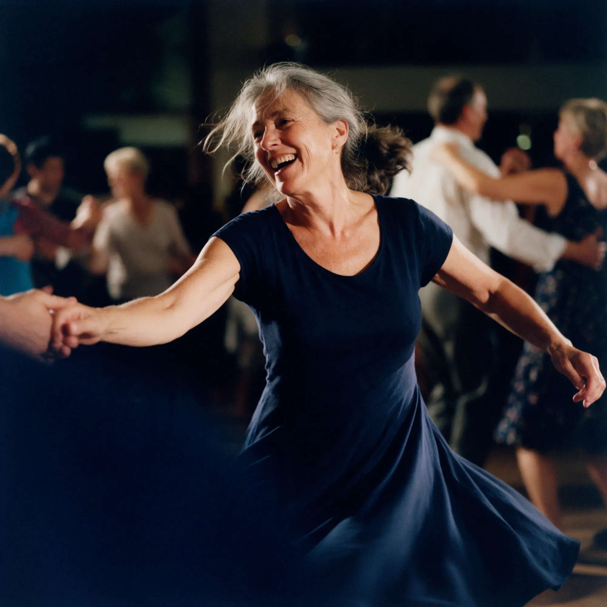 A woman in her early sixties laughing mid-turn on a social dance floor
